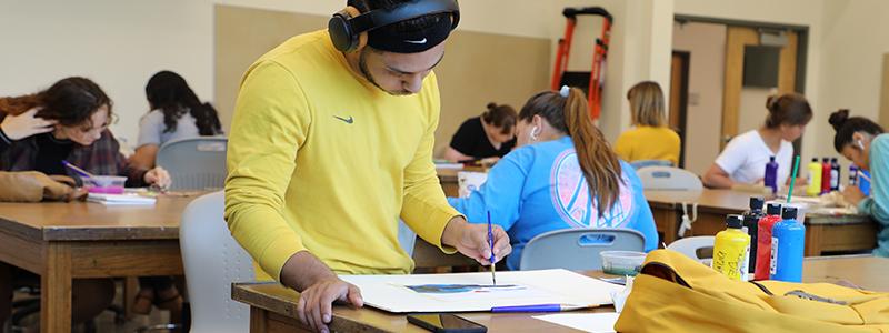 Male student drawing on paper on a table.