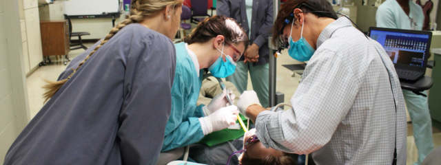 Man and Two Women Hover Over Patient in Chair