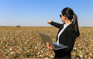 Woman Holding Laptop and Pointing to a Field of Crops