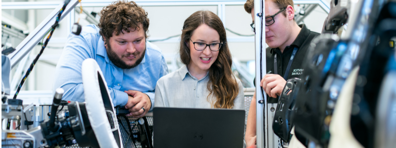 Three People Working on Computer and Surrounded by Machinery